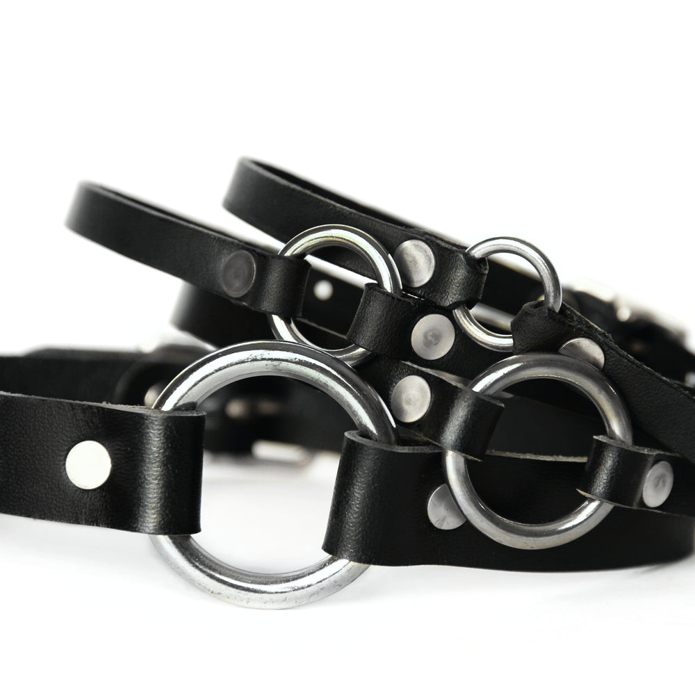 Four black leather chokers sit piled upon one another in largest to smallest order. 