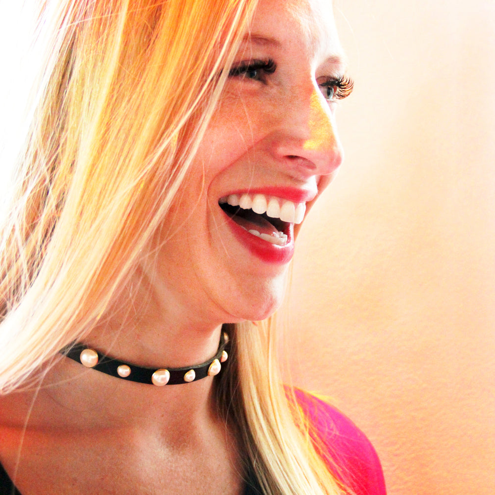 Model in red lipstick laughs exuberantly while wearing a thin, black choker studded with pearls around their neck.