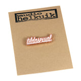 Tildasexual pin pinned to a branded paper backing. Brand name, Audio Helkuik, is stamped in black onto tan paper.