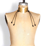 A metallic gold version of the Laced Front Choker is shown on a dress form. The leather shines in the light. Laces are black.