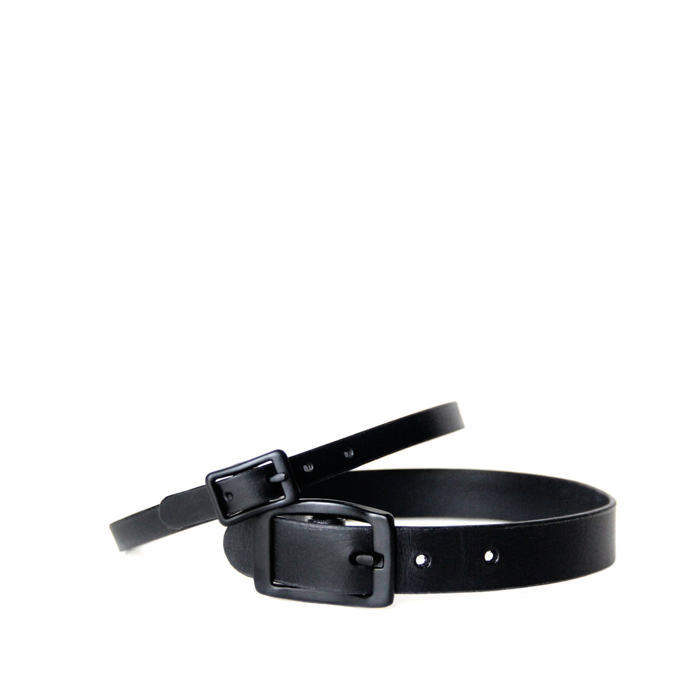 A thin black choker is propped up on a thicker black choker. Both have black buckles.