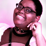 A pink-toned image of a model smiling in a mesh top while wearing a leather harness and leather choker. 