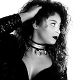 Black and white photo of a curly-haired femme model wearing a black bra, dark lipstick and a triple ring choker.