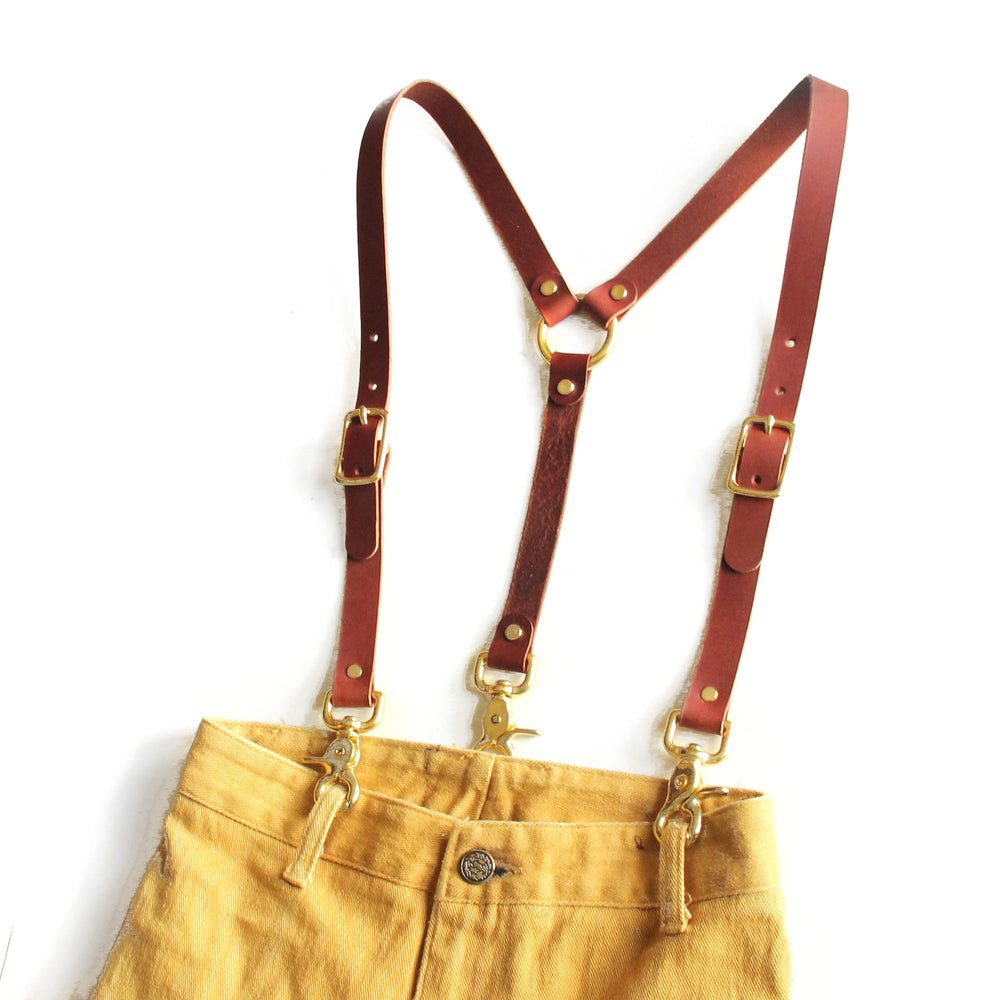 Chestnut brown leather high-waisted suspenders, with swivel trigger clips and brass hardware on pants