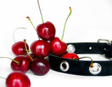 Close up of grommeted choker covered in a pile of shiny red cherries.