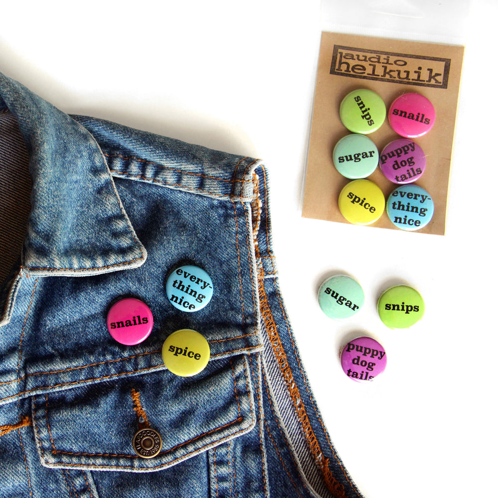 Denim vest adorned with snails, spice, and everything nice pins from the confetti colorway. The rest of the pins lay nearby.