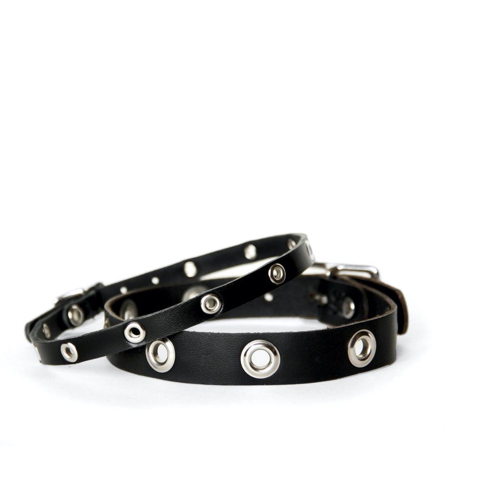 Two black leather chokers laying on top of one another. One is thin and one is wider leather. Both have grommets.