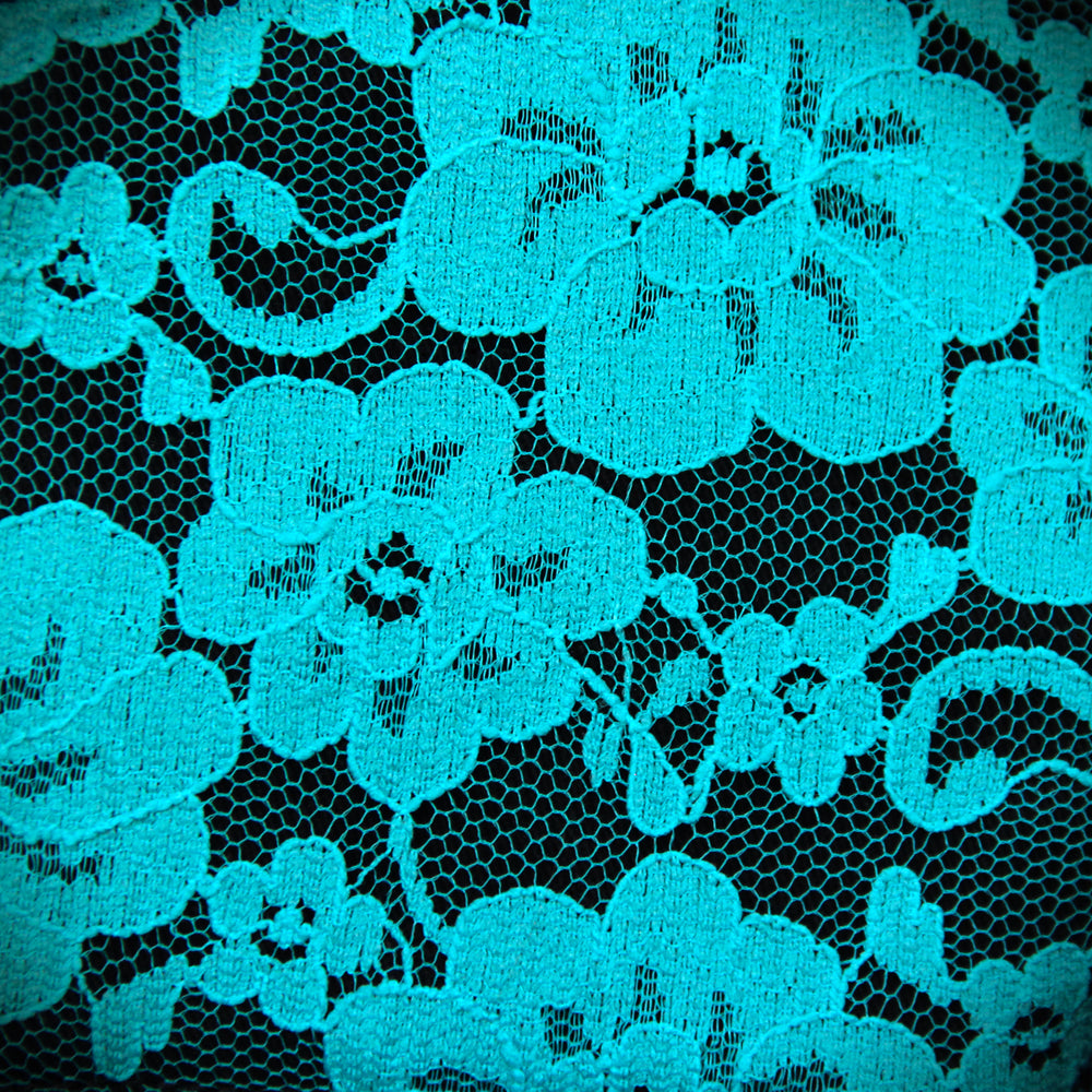 Closeup of teal lace layered over black cotton fabric. Lace is a floral design.