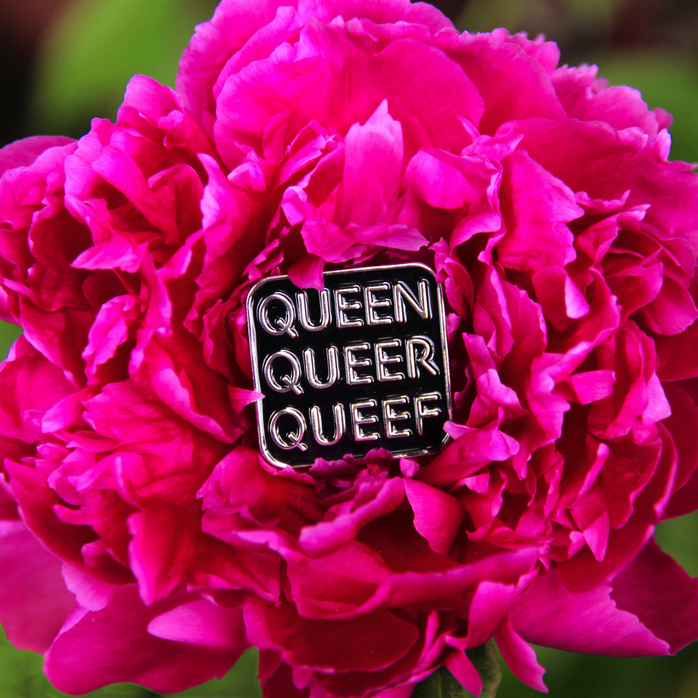 A bright magenta peony in full bloom holds a Q-words pin. The pin is nestled in the center of the flower’s petals.