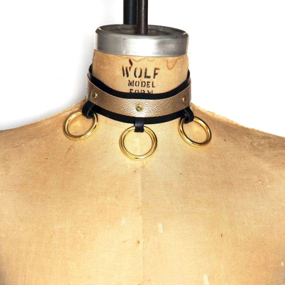 Dressform adorned with a black leather collar with beige metallic contrast leather. Choker has three bright brass o-rings at the front.